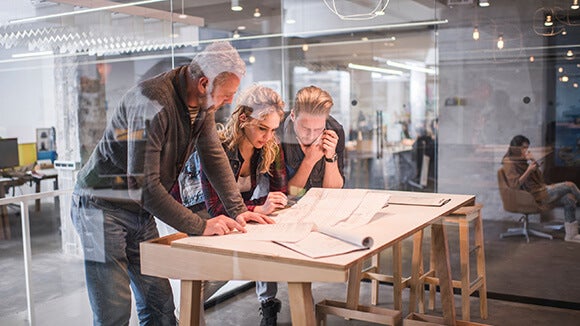 Trois personnes debout qui travaillent sur une table derrière une vitre