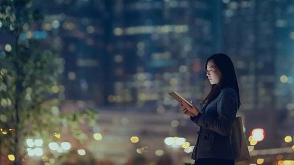 Une femme regarde sa tablette dans la rue éclairée