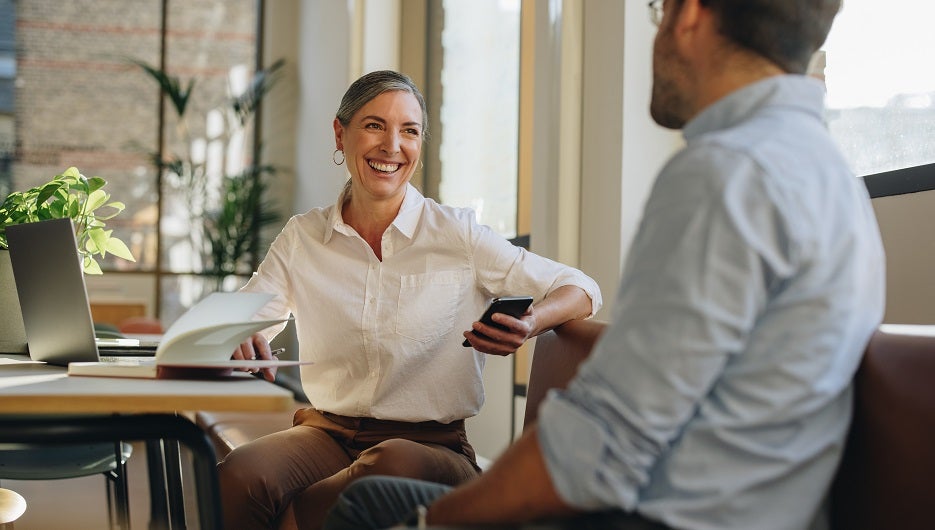 Woman talking with coworker at office desk. Businesswoman having discussion with team member in office.