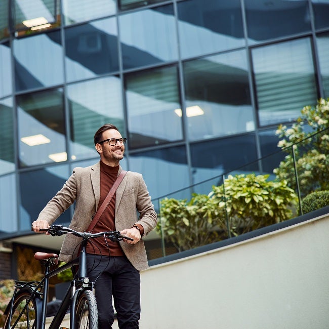 A cheerful businessman pushing his bicycle and going home from work, looking satisfied.